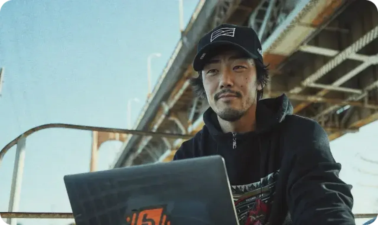 A man sitting using a laptop, with the bridge in the background.